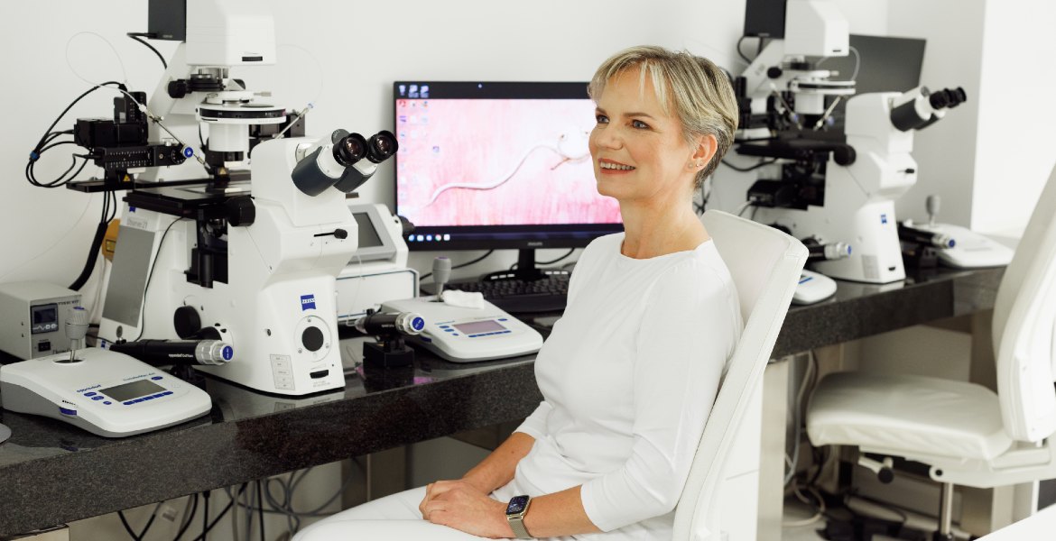 MSc Renata Hüttelova in un laboratorio IVF, seduta vicino a microscopi e apparecchiature per test della fertilità, dispositivi Zeiss visibili sulla scrivania.