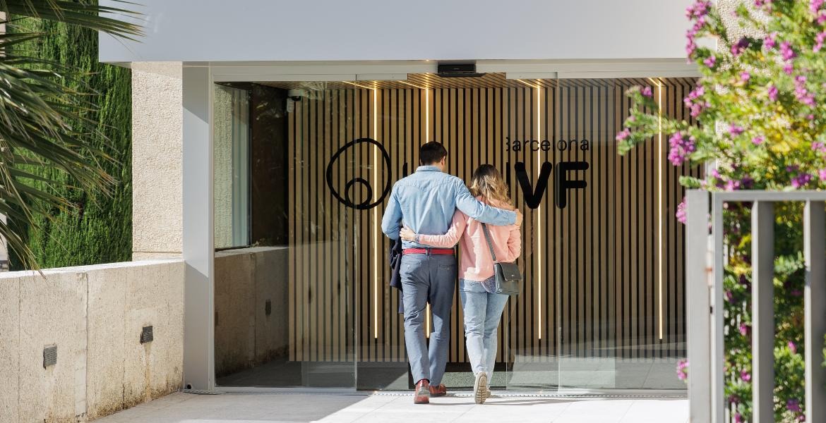 Coppia entra insieme nell’ingresso della clinica Barcelona IVF, centro moderno per trattamenti di fertilità in Spagna.