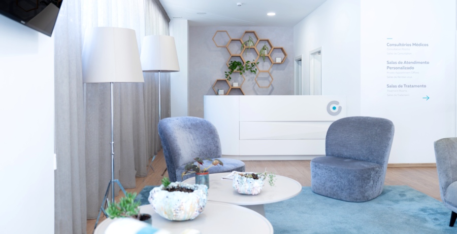 Accogliente sala d’attesa della clinica di fertilità Ferticentro a Coimbra con poltrone grigie, tavolini bassi, reception bianca e arredi di design